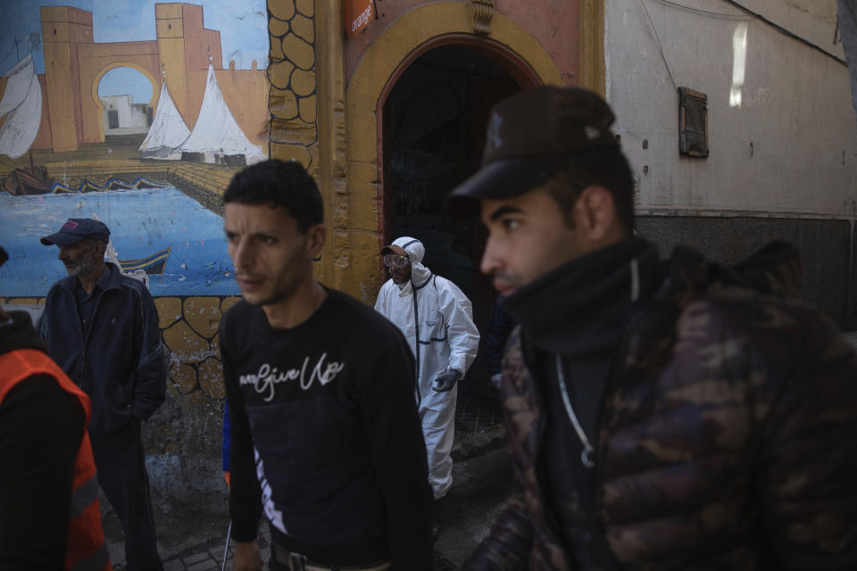 In this in Wednesday, March 25, 2020 photo, volunteers and residents walk outside the entrance of a housing complex in Sale, near Rabat, Morocco. Hundreds of people live in crowded rooms in this Moroccan housing complex with no running water and no income left because of the coronavirus lockdown measures. However volunteers come to help clean as the government tries to protect the population from virus while not punishing the poor. (AP Photo/Mosa'ab Elshamy)