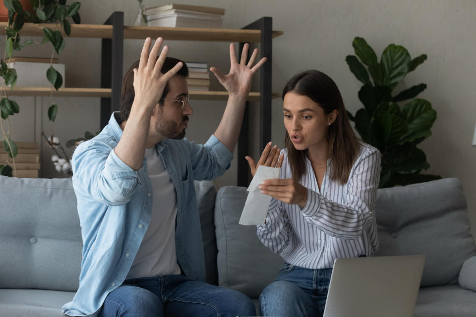 Two people sitting on a couch with animated expressions, one holding a document and both gesturing in surprise or conversation