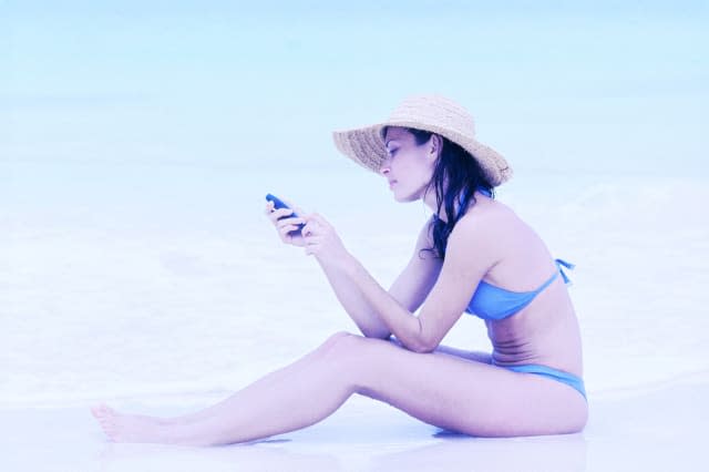 tungsten shot of a young woman sitting on the beach operating a mobile phone