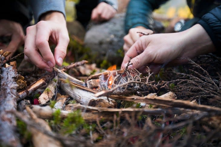 Close-up of hands adding twigs to a small flame. 