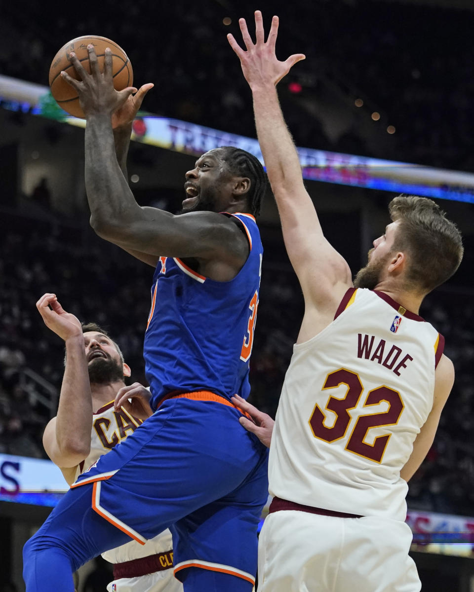 New York Knicks' Julius Randle, center, drives to the basket against Cleveland Cavaliers' Kevin Love, left, and Dean Wade in the second half of an NBA basketball game, Monday, Jan. 24, 2022, in Cleveland. The Cavaliers won 95-93. (AP Photo/Tony Dejak)