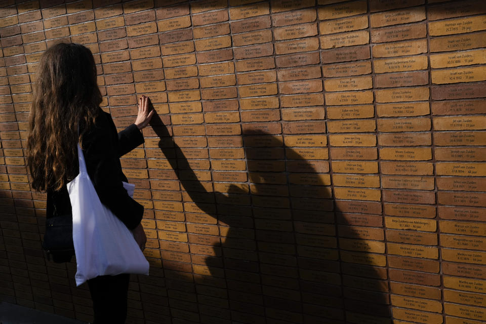 A woman touches one of the name stones after King Willem-Alexander officially unveiled a new monument in the heart of Amsterdam's historic Jewish Quarter on Sunday, Sept. 19, 2021, honoring the 102,000 Dutch victims of the Holocaust. Designed by Polish-Jewish architect Daniel Libeskind, the memorial is made up of walls shaped to form four Hebrew letters spelling out a word that translates as "In Memory Of." The walls are built using bricks each of which is inscribed with the name of one of the 102,000 Jews, Roma and Sinti who were murdered in Nazi concentration camps during World War II or who died on their way to the camps. (AP Photo/Peter Dejong)