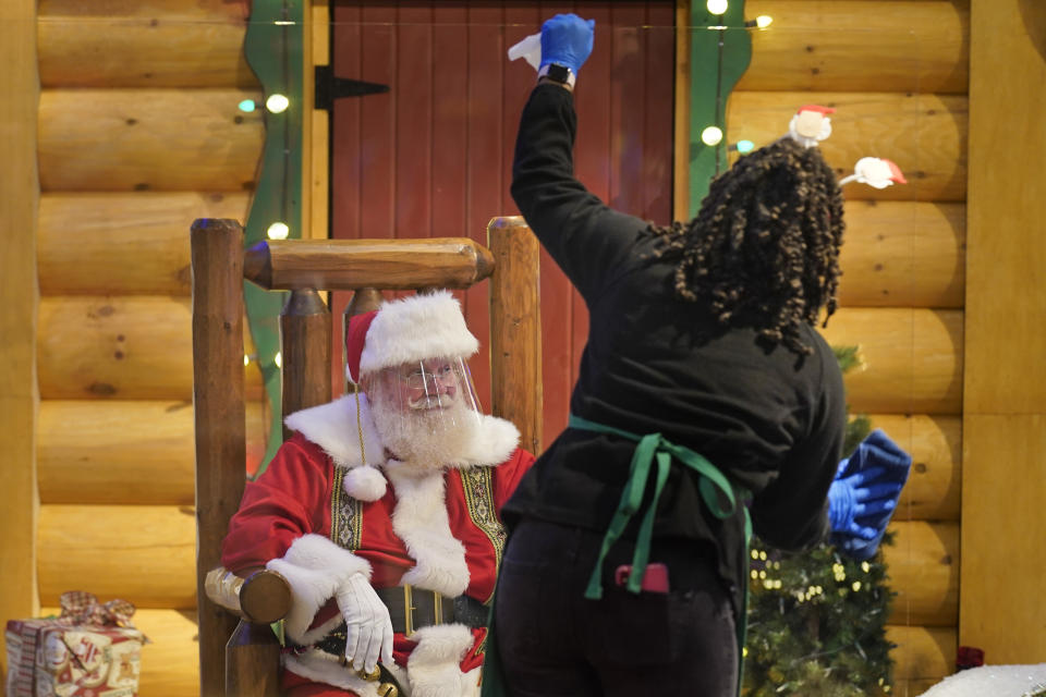 LaToya Booker cleans a transparent barrier between visitors for Santa at a Bass Pro Shop in Bridgeport, Conn., on Nov. 10, 2020. In this socially distant holiday season, Santa Claus is still coming to towns (and shopping malls) across America but with a few 2020 rules in effect. (AP Photo/Seth Wenig)