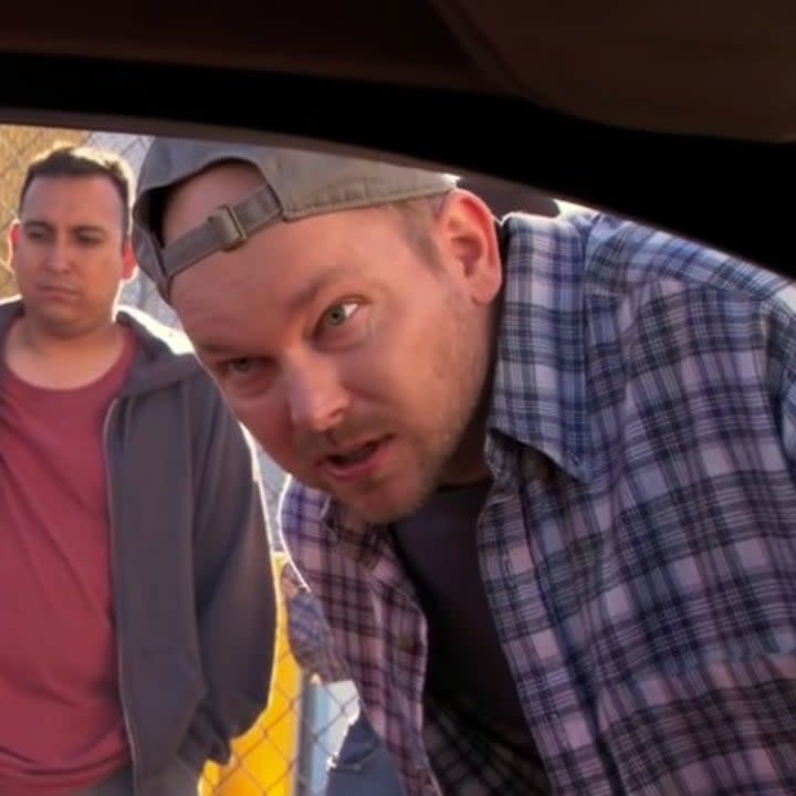 A man leans into an open car window while other men stand behind him