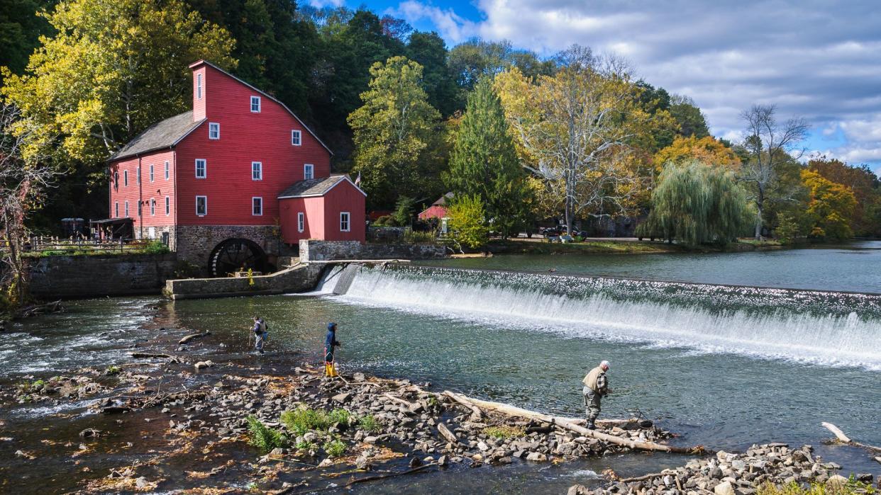 Clinton, New Jersey, USA - October 17, 2015: Three fishermen with rods, nets, and boots fish in the shallow waters below the dam at the Old Red Mill  on a crisp Autumn afternoon.