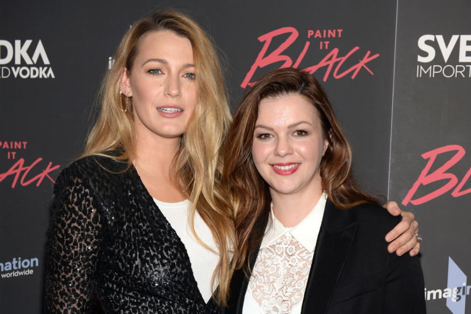 Two women posing together at an event, one in a lace top, the other in a blazer