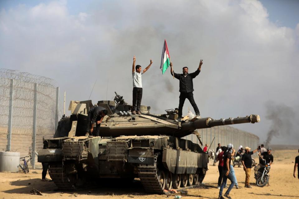 Palestinians wave their national flag and celebrate by a destroyed Israeli tank at the Gaza Strip fence (AP)