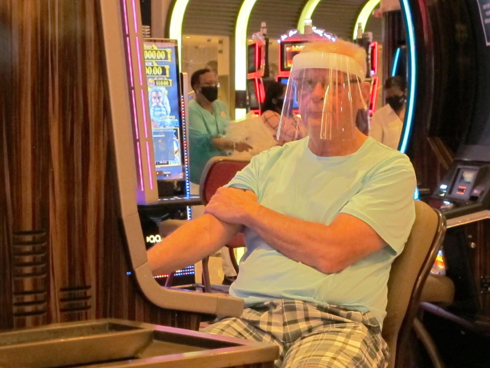 A gambler wears a face shield while playing a slot machine at the Hard Rock casino in Atlantic City N.J. on July 2, 2020, the first day it was allowed to reopen during the coronavirus pandemic. Figures released on April 9, 2021 show Atlantic City's nine casinos collectively saw their gross operating profits decline by more than 80% in 2020.(AP Photo/Wayne Parry)