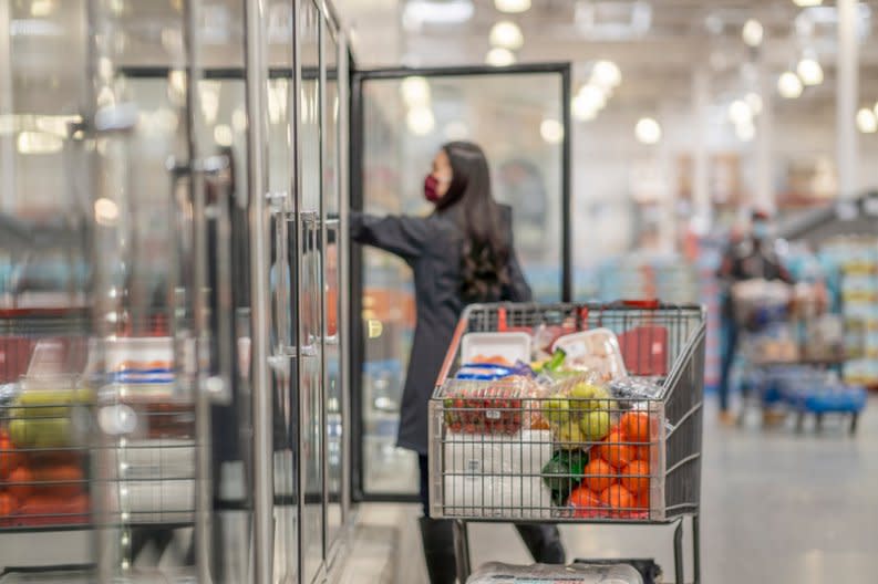 A person shopping in the freezer aisle with a cart full of groceries.