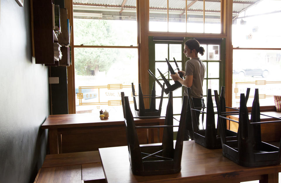 Worker stacks chairs on table in cafe