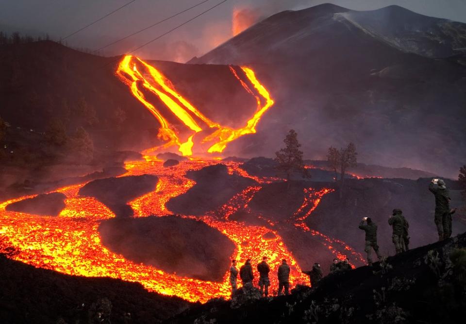 Spanish Army soldiers stand on a hill as lava flows as volcano continues to erupt on the Canary island of La Palma (AP)