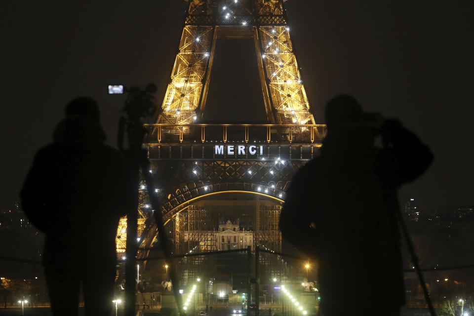 Cameramen stand in front of the Eiffel Tower where the word "Merci", the French word for 'Thank you", is emblazoned as France's coronavirus death toll continued to climb, in Paris, Friday, March 27, 2020. Health workers fighting to save lives in France from COVID-19 have received a huge show of gratitude, from the Eiffel Tower. The new coronavirus causes mild or moderate symptoms for most people, but for some, especially older adults and people with existing health problems, it can cause more severe illness or death. (AP Photo/Thibault Camus)