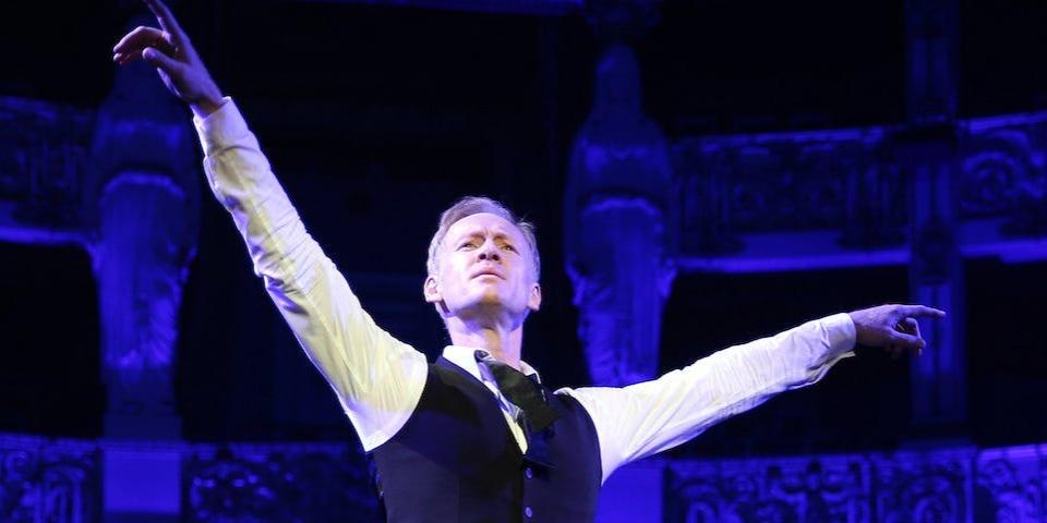 German ballet director Igor Zelensky pictured with arms raised on stage, with blue lighting behind him, in 2018.