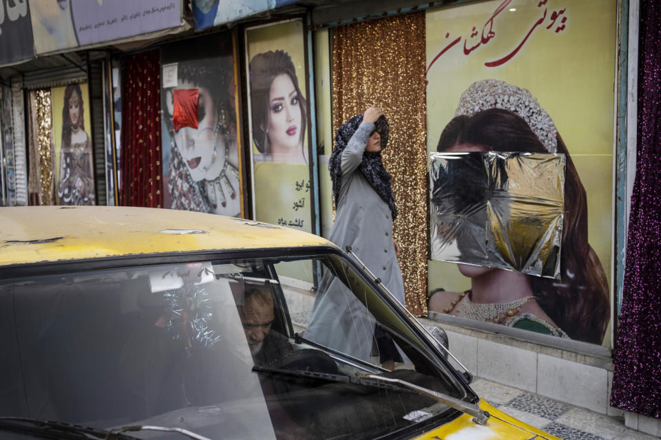 FILE - A woman walks past beauty salons with window decorations which have been defaced in Kabul, Afghanistan, Sunday, Sept. 12, 2021. A spokesman at Afghanistan's Vice and Virtue Ministry said Tuesday, July 4, 2023, the Taliban are banning women's beauty salons. (AP Photo/Bernat Armangue, File)