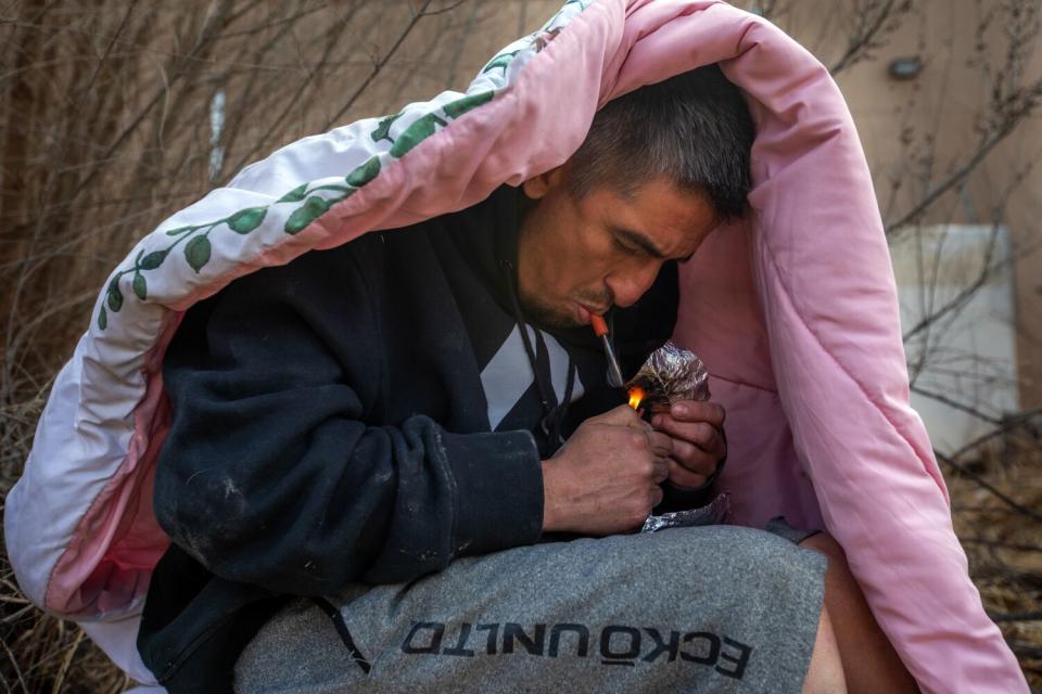 A man under a blanket lights a pipe.