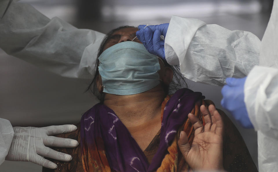 Health workers takes a nasal swab sample of a woman passenger to test for COVID-19 at a train station in Mumbai, India, Friday, Nov. 27, 2020. India has more than 9 million cases of coronavirus, second behind the United States. (AP Photo/Rafiq Maqbool)