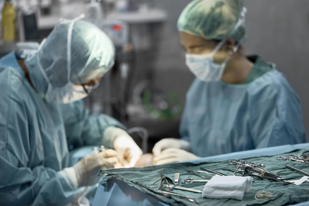 Close-up of medical instruments with doctors performing surgery in background. Male and female surgeons are operating dog in hospital. Veterinarians are in scrubs at animal clinic.