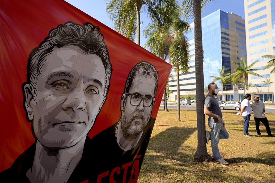 Workers of the National Indian Foundation, FUNAI, stand next to a banner with images of missing Indigenous expert Bruno Pereira, right, and freelance British journalist Dom Phillips, during a vigil in Brasilia, Brazil, Monday, June 13, 2022. Brazilian police are still searching for Pereira and Phillips, who went missing in a remote area of Brazil's Amazon a week ago. (AP Photo/Eraldo Peres)