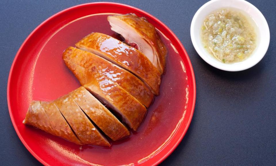 A round red plate with an amber-coloured crescent of chicken and a small white dip dish next to it