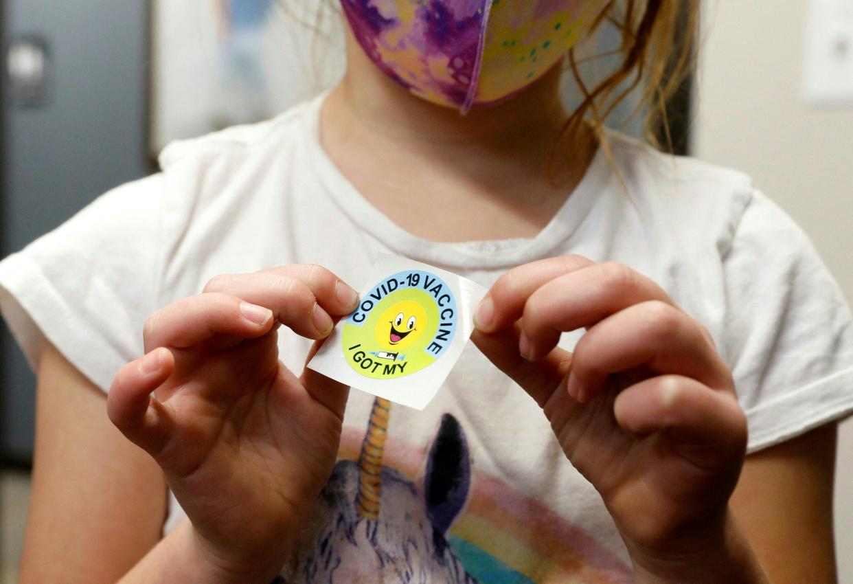 A youngster with a mask shows off a sticker noting her COVID vaccination.