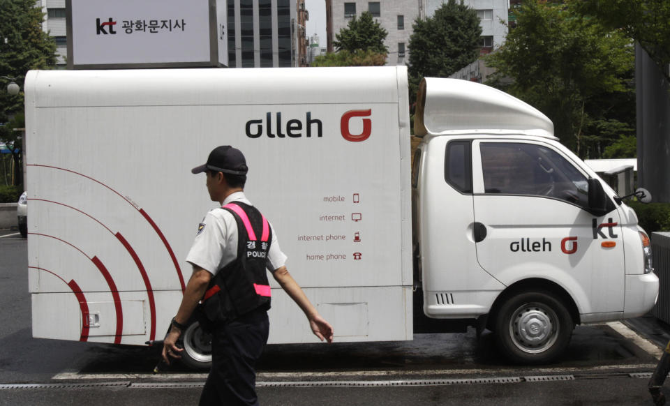 A police officer passes by a vehicle advertising KT, South Korea's largest fixed-line telephone company and No. 2 mobile operator, at the company's branch office in Seoul, South Korea, Monday, July 30, 2012. South Korean police Sunday said they arrested two men who allegedly stole the personal details of about 8 million KT mobile phone subscribers and sold the data to marketing companies in one of the country's biggest hacking schemes.(AP Photo/Ahn Young-joon)