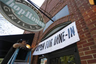 Jason Godbey hangs a banner over the entrance of Madison Chop House Grille as they prepare to shift from take out only to dine-in service Monday, April 27, 2020, in Madison, Ga. Gov. Brian Kemp eased restrictions on restaurants as long as guide lines are followed to prevent to spread of the coronavirus. (AP Photo/John Bazemore)