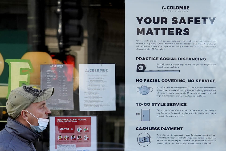 FILE - In this Nov. 12, 2020, file photo, a man walks past a coffee shop as the store displays information signs in Chicago. An increasing number of governors and mayors are imposing restrictions ahead of Thanksgiving for fear that holiday travel and family gatherings will only worsen the record-breaking, coast-to-coast resurgence of the coronavirus. (AP Photo/Nam Y. Huh, File)