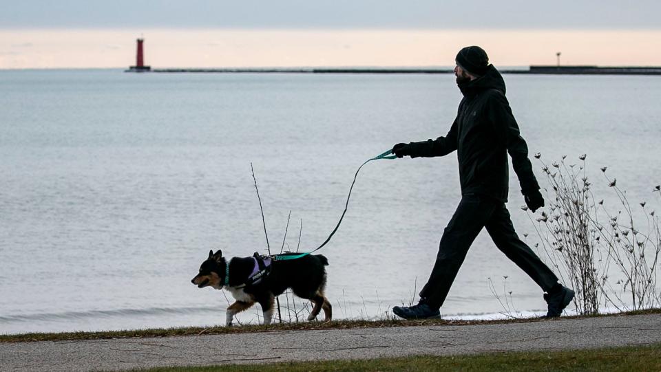 A man is silhouetted with his dog as he walks along the Sheboygan lakefront along Broughton Drive in December 2021.
