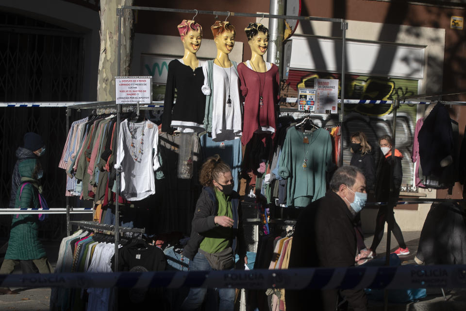 People walk by a clothes stall in the Rastro flea market in Madrid, Spain, Sunday, Nov. 22, 2020. Madrid's ancient and emblematic Rastro flea market reopened Sunday after a contentious eight-month closure because of the COVID-19 pandemic that has walloped the Spanish capital. (AP Photo/Paul White)