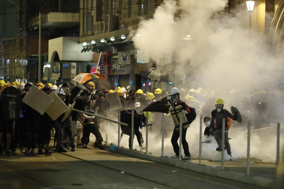 FILE - In this file photo taken Sunday, July 21, 2019, protesters react to teargas as they confront riot police officers in Hong Kong. Hong Kong, a former British colony, was returned to China in 1997 under a “one country, two systems” concept that gives the city a fair degree of autonomy over its affairs, but China may intervene to quell protests now in their seventh week. (AP Photo/Vincent Yu, File)