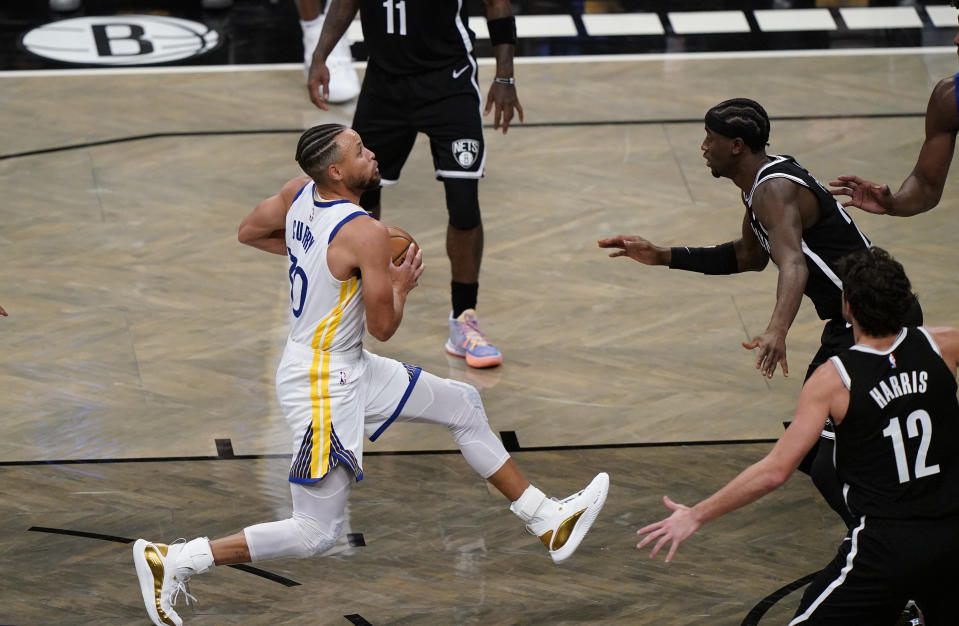 Golden State Warriors guard Stephen Curry (30) drives to the basket with Brooklyn Nets guard Caris LeVert (22) and Joe Harris (12) defending during the 2nd quarter of an opening night NBA basketball game, Tuesday, Dec. 22, 2020, in New York. (AP Photo/Kathy Willens)