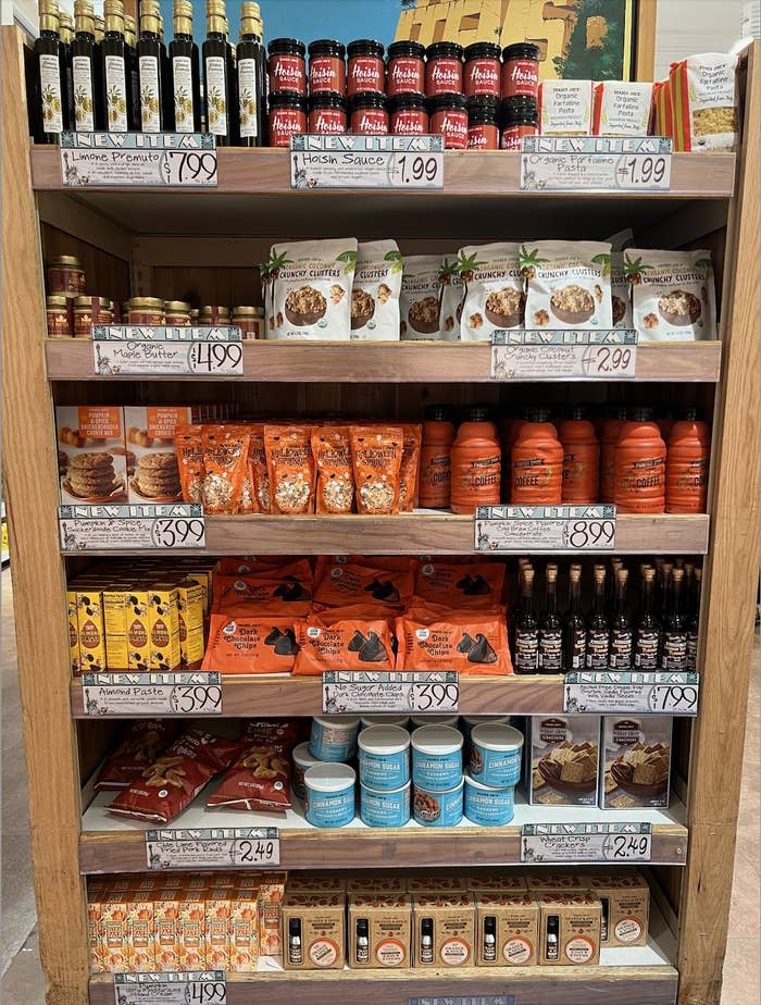 A supermarket shelf displaying various food products, including pasta sauce, olive oil, cookies, pancake mix, cinnamon rolls, and other snacks