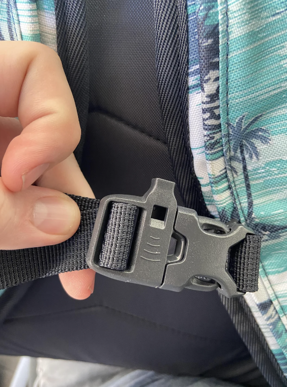 Close-up of a hand adjusting a plastic buckle on the strap of a patterned backpack