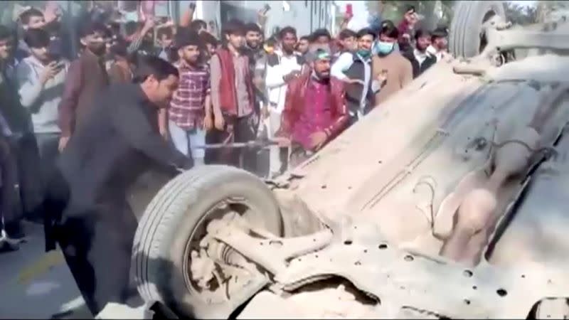 A mob hits an overturned car with sticks after an attack on a factory in Sialkot