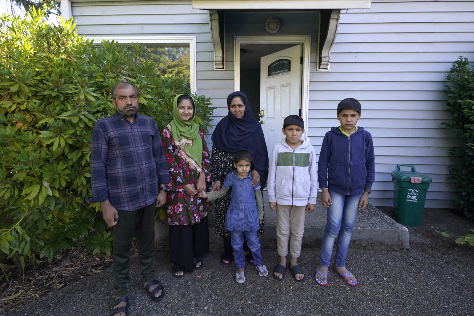 Abdul, left, who worked as a mechanic before he left Kabul, Afghanistan with his family about a month ago, poses for a photo, Thursday, Sept. 16, 2021, with his family in front of a rental house where they have been provided a place to stay in Seattle. The home is owned by Thuy Do, who was nine years old when her family arrived in the United States from Vietnam in the 1980s. Now Do and her husband have offered their vacant rental home to refugee resettlement groups to house newly arriving Afghans in need of a place to stay. (AP Photo/Ted S. Warren)