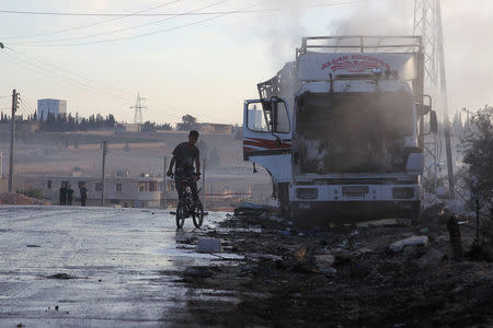 A boy rides a bicycle near a damaged aid truck after an airstrike on the rebel held Urm al-Kubra town, western Aleppo city. REUTERS/Ammar Abdullah