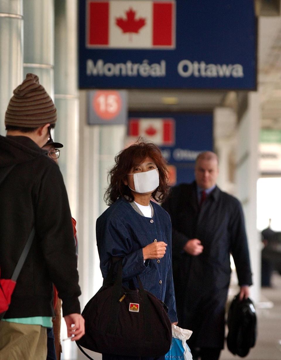 A passenger wears a face mask to protect against the SARS virus, while waiting for a shuttle outside Pearson International Airport in Toronto, Canada, Wednesday, April 23, 2003.  (AP Photo/CP/Globe and Mail, J.P. Moczulski) ORG XMIT: CPT120