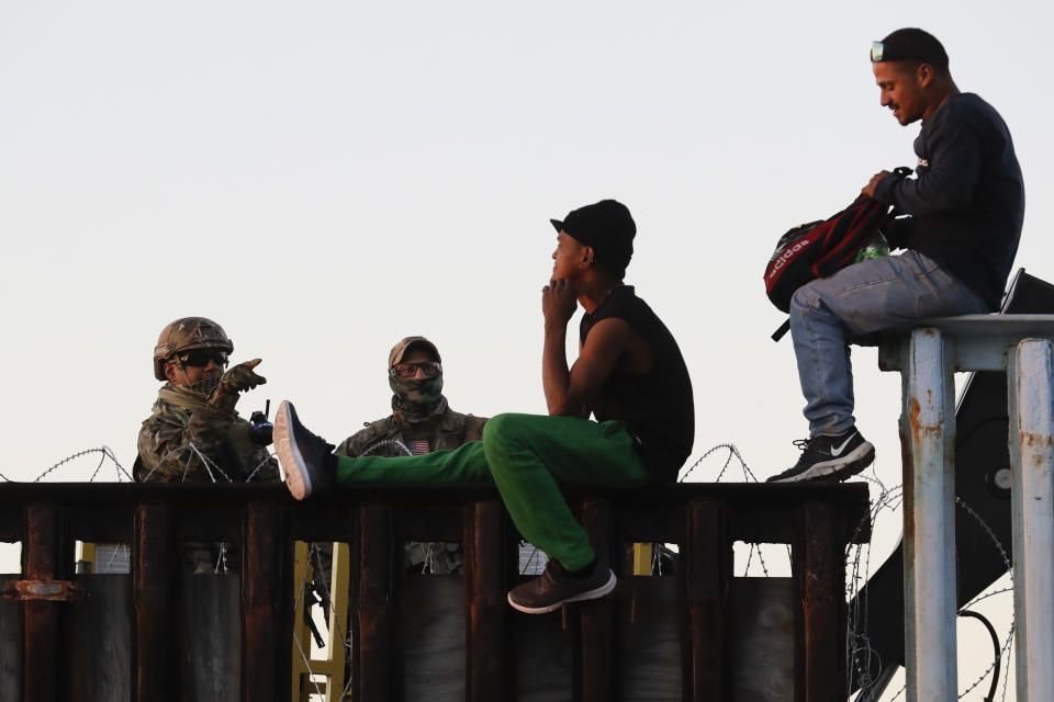 Agentes de la Patrulla Fronteriza de Estados Unidos (izquierda) hablan con dos migrantes centroamericanos sentados sobre la estructura que separa México de Estados Unidos, el 14 de noviembre de 2018, en Tijuana, México. (AP Foto/Gregory Bull)