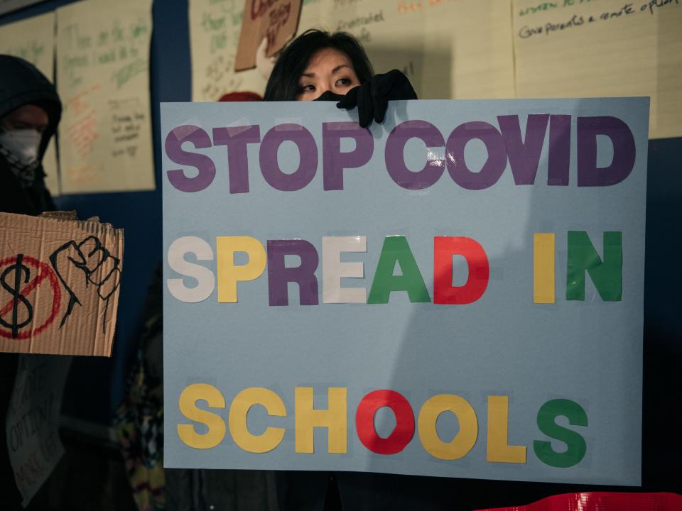 a teacher holds a sign that says "STOP COVID SPREAD IN SCHOOLS" at a NYC protest over COVID-19 in schools