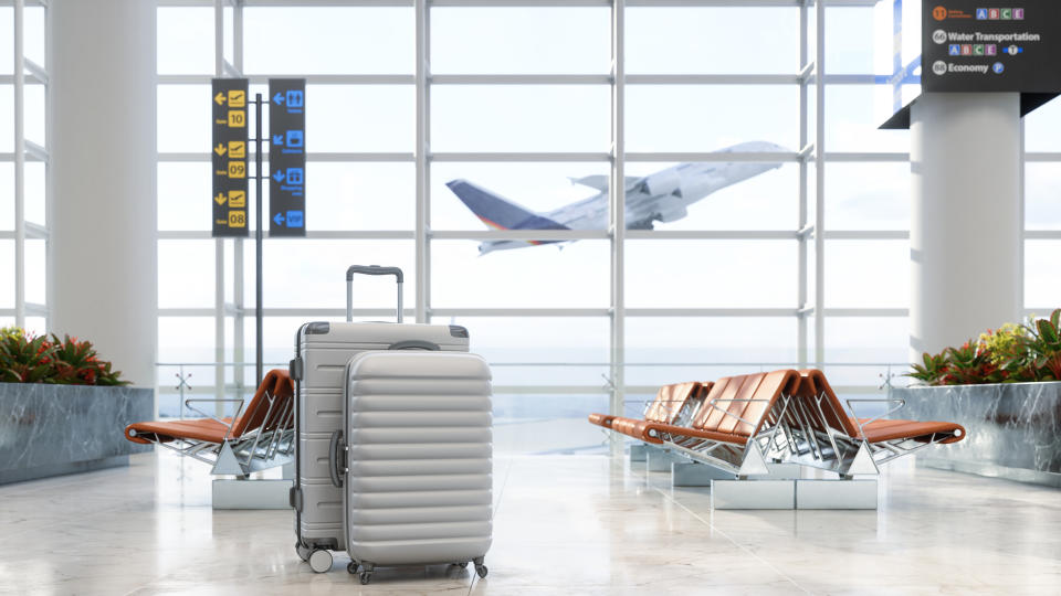 Luggage in an open airport terminal with an airplane taking off in the background. No people in the scene