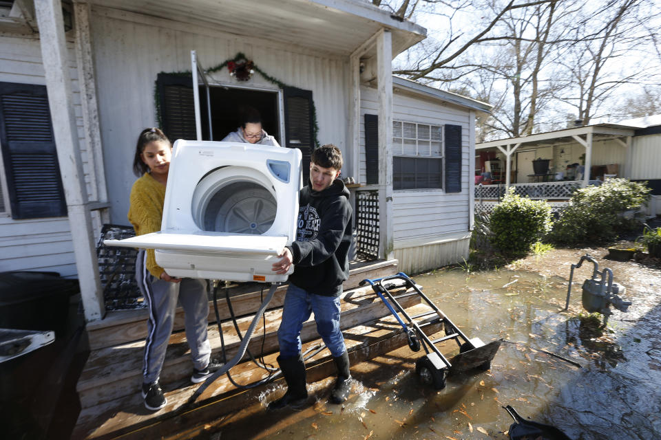 Mario Vargas, right, his sister Alondra Rodriguez, left, and their aunt Nadia Castillo, back, carry a washing machine from Vargas' mother's mobile home in the Harbor Pines Mobile Home Community of Ridgeland, Miss., Friday, Feb. 14, 2020. Officials estimate the flooding along the Pearl River to create the worst flooding in the Capitol city of Jackson and some neighboring communities since 1983. (AP Photo/Rogelio V. Solis)