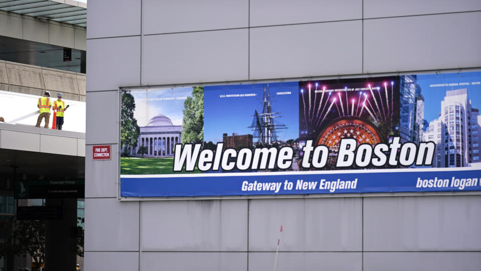 A "Welcome to Boston" sign hangs on the facade of a structure as two workers assemble a portion of a roof at Terminal E, where most international flights arrive and depart, at Logan Airport in Boston, Tuesday, Sept. 29, 2020. Homeless families and individuals will be barred from sleeping overnight at Logan International Airport, beginning July 9, state officials said Friday, June 28, 2024. (AP Photo/Charles Krupa, File)