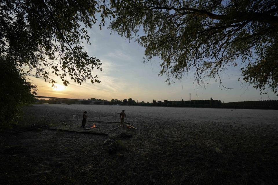 Boys light a fire at sunset with wooden pieces, in Boretto, on the bed of the Po river, Italy, Tuesday, June 14, 2022. The drying up of the river is jeopardizing drinking water in Italy's densely populated and highly industrialized districts and threatening irrigation in the most intensively farmed part of the country. (AP Photo/Luca Bruno)