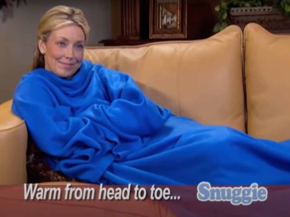 Woman in a Snuggie blanket on a couch, text advertises being 'Warm from head to toe'