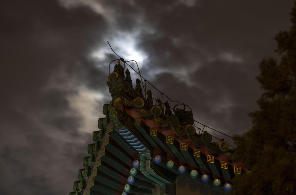 Roof decorations depicting mythical sacred beasts are silhouetted near a penumbral lunar eclipse blocked by clouds during the early hours of Saturday, May 6, 2023 in Beijing. (AP Photo/Ng Han Guan)