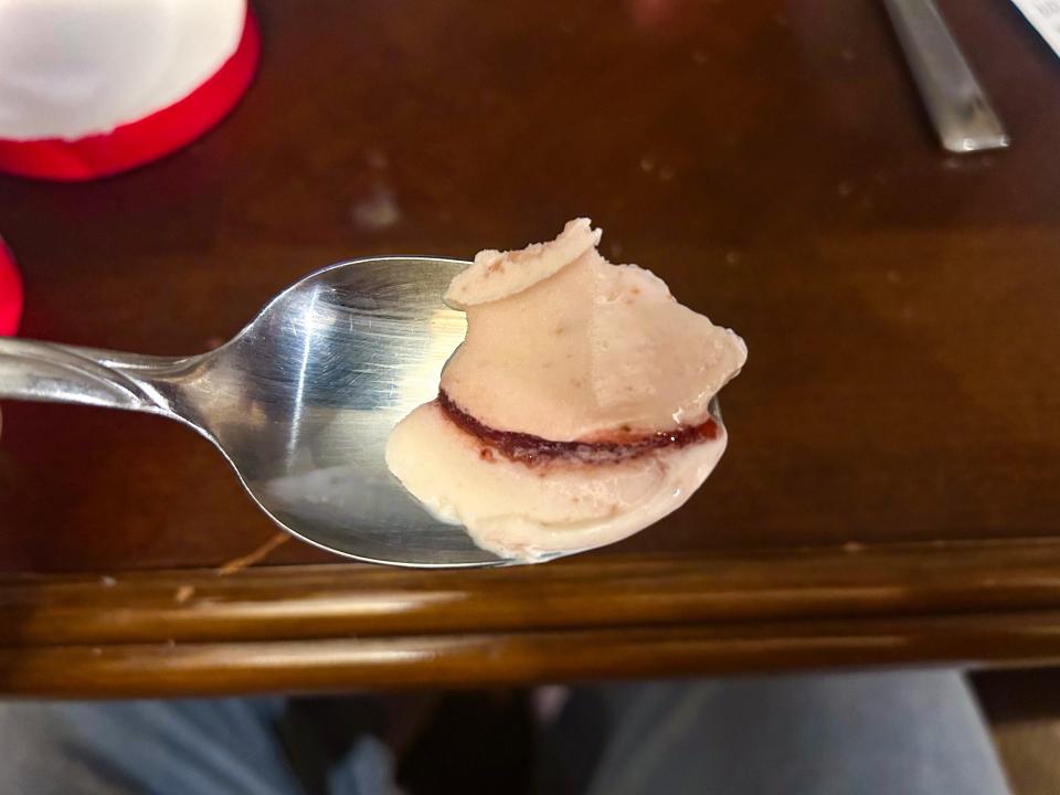 A metal spoonful of light-pink ice cream with a dark-red strawberry swirl in it