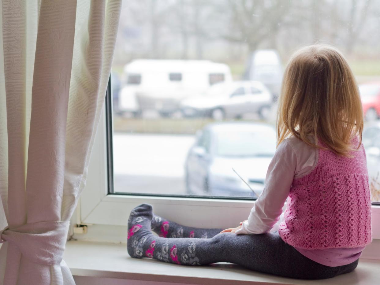 Little girl sitting on window sill looking out of window