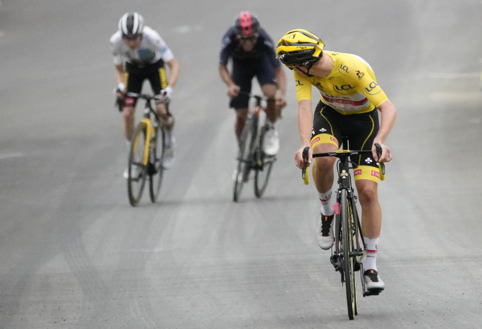 Slovenia's Tadej Pogacar, wearing the overall leader's yellow jersey, looks back to check if he has enough lead on Denmark's Jonas Vingegaard, wearing the best young rider's white jersey, and Richard Carapaz of Ecuador , as he crosses the finish line to win the eighteenth stage of the Tour de France cycling race over 129.7 kilometers (80.6 miles) with start in Pau and finish in Luz Ardiden, France,Thursday, July 15, 2021. (AP Photo/Christophe Ena)