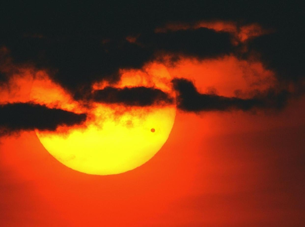 The sun rises through a bank of clouds over the East River of Manhattan as the planet Venus (dot on lower right of sun) crosses its face, 08 June, 2004, in New York: STAN HONDA/AFP via Getty Images