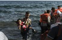 A Syrian refugee carries a child out of an inflatable boat on Lesbos island